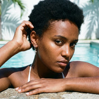 Thumbnail for Pave Cross Huggie Hoops in Silver, worn by a tropical pool | SKU: 41006-silver