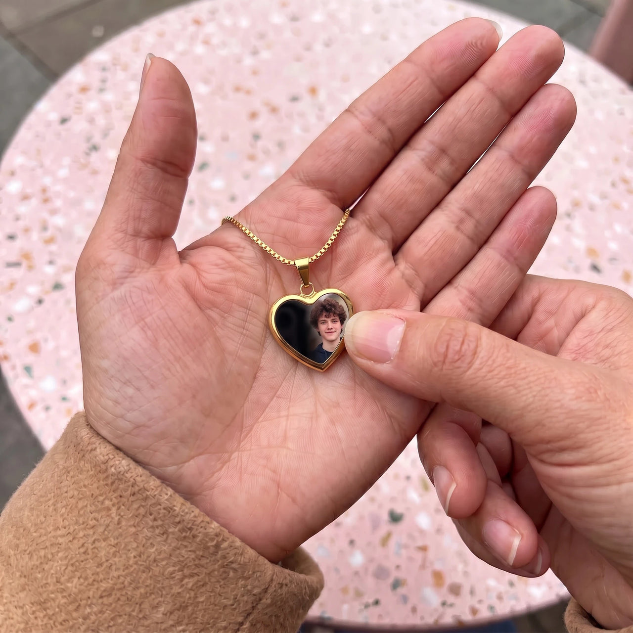 Thumb warming the gold heart pendant: the hidden photo appears under the thumb while the rest stays black | SKU: TPH-CHTN-GOLD-SMALL