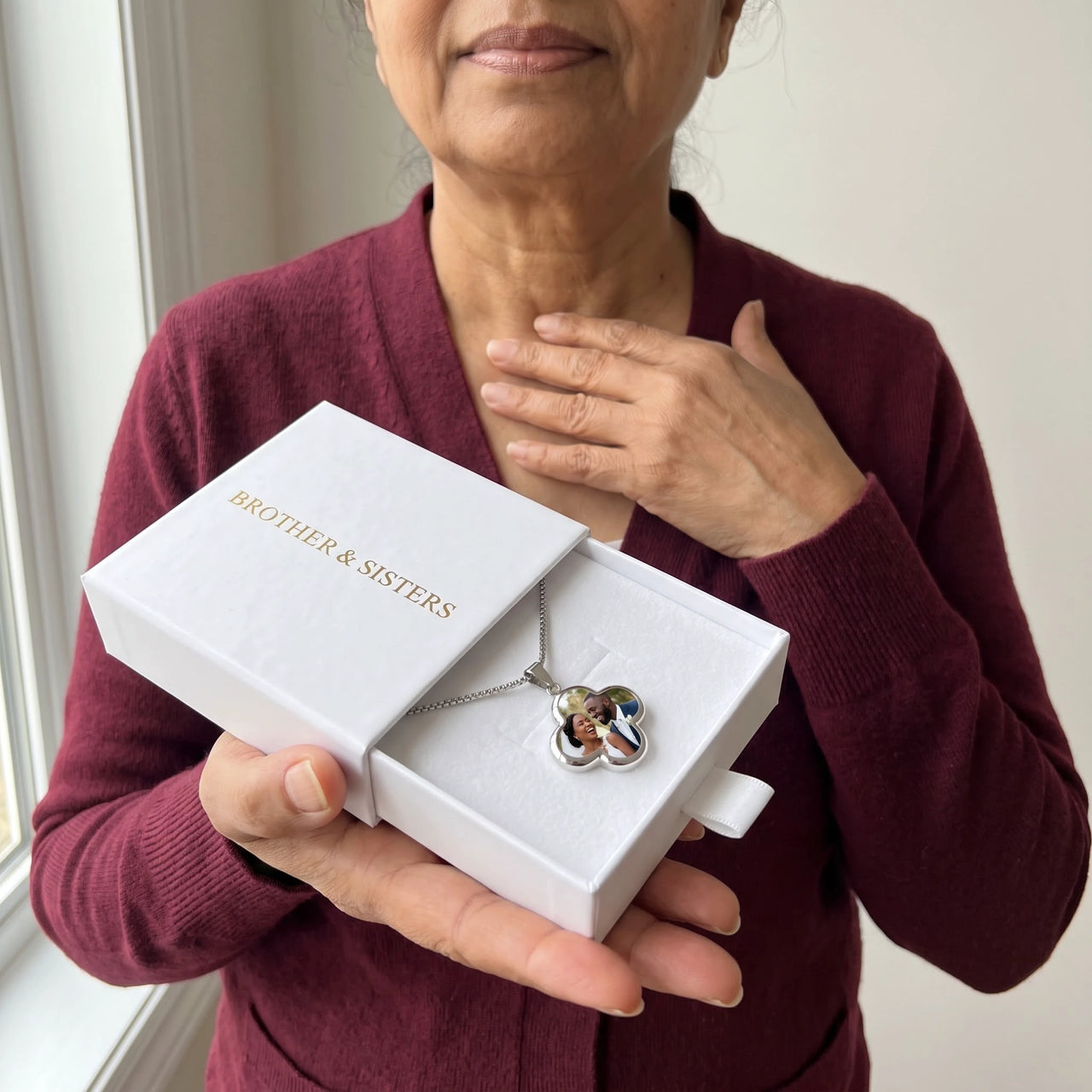 Woman in a burgundy cardigan holding the Brother & Sisters gift box with the silver clover photo necklace inside | SKU: TPH-CLVN-SILVER