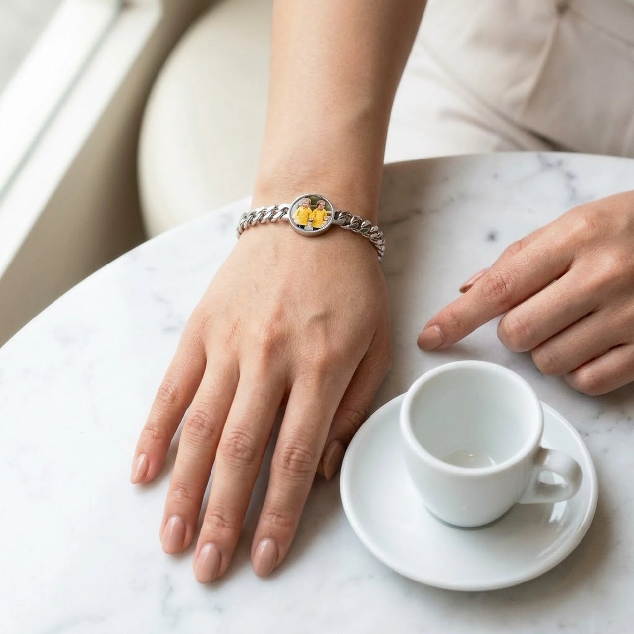 The silver round photo bracelet on her wrist at a cafe table, showing its real small size | SKU: TPH-RNDB-SILVER